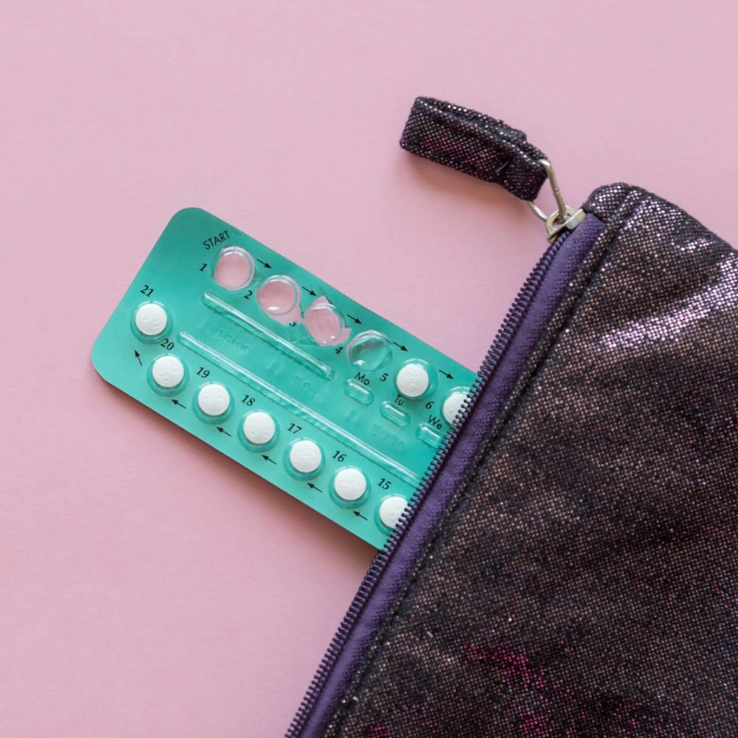 Shot of a birth control packet with four pills taken slightly coming out of a little purple bag.