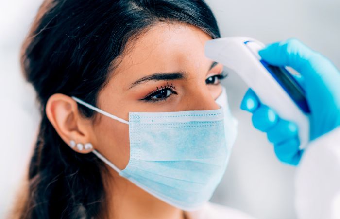 Woman with mask of getting her temperature tested.