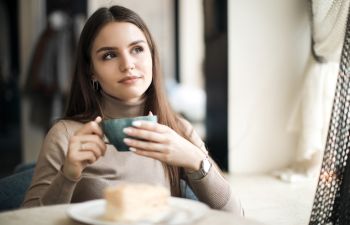 Woman with long hair is sitting and drinking coffee or tea.