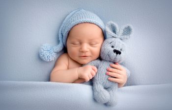 A cute newborn boy in the first days of life sleeps gently hugging a light blue knitted bunny.