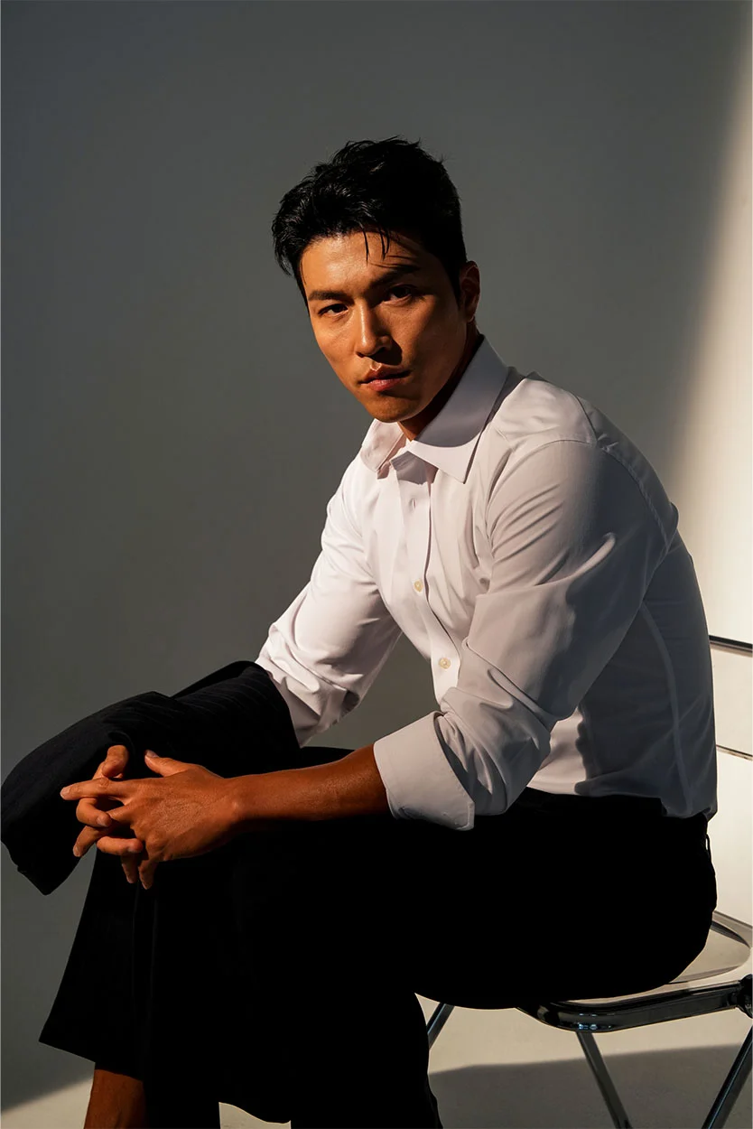 A serious man with dark hair, wearing a white collared shirt and black pants, is sitting on a chair with dramatic side lighting. - Cystic Fibrosis in New York, NY