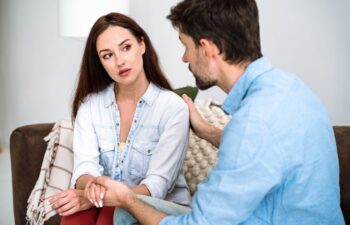 Young man giving support for woman, expressing empathy, hugging for shoulder. Honest conversation in marriage. Overcoming crisis in couple together.